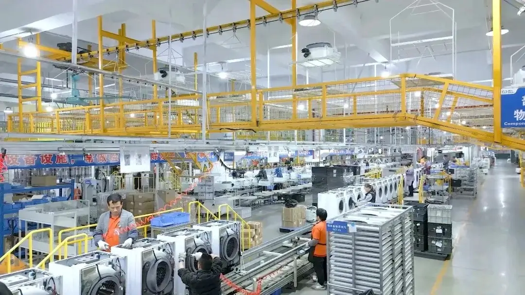 Modern Hovm factory workshop with front-load washing machine assembly line and aerial material conveyor system.